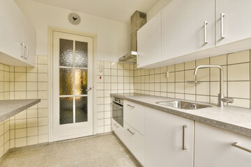 A sleek, modern kitchen showcasing minimalist white cabinetry and simple design. The space features light-colored countertops and a glass-paneled door enhancing light flow.