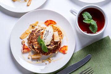 Cottage cheese pancakes with orange and chia seeds on a white plate with a cup of tea and mint on a light background. The concept of a healthy, dietary breakfast at home.
