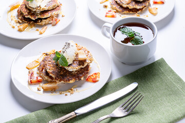 Cottage cheese pancakes with orange and chia seeds on a white plate with a cup of tea and mint on a light background. The concept of a healthy, dietary breakfast at home.
