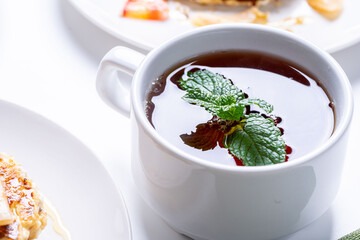 A cup of tea with a sprig of mint, close-up. A white cup with a thirst-quenching drink.