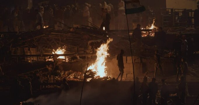 Varanasi, Uttar Pradesh, India. Cremation in process on Manikarnika Ghat. Cinematic Camera movement moving along riverbank embankment. View from riverside. night lights. Fire, smoke - Funeral rites of