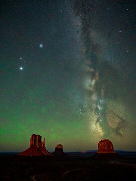 a captivating night sky over Monument Valley, showcasing the Milky Way's vivid glow. The silhouetted rock formations add depth, blending natural wonder with serene celestial beauty.
