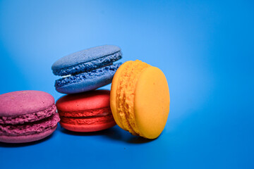 Four colorful macarons—purple, red, blue, and yellow—arranged playfully on a vibrant blue background, showcasing their soft texture and vibrant pastel tones