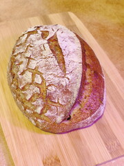 freshly baked artisanal whole wheat sourdough bread with rustic crust cooling on a wooden board surface front view