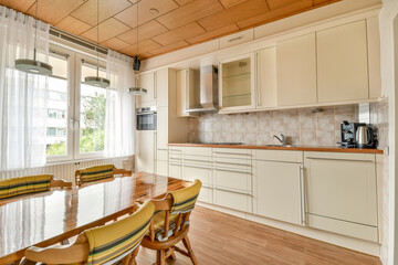 A sleek modern kitchen featuring warm tones, large windows allowing natural light, and a minimalist design with wooden elements and ample storage space.