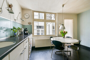 A stylish modern kitchen featuring a round dining table, minimalist decor, and large windows allowing ample natural light, creating an inviting atmosphere.