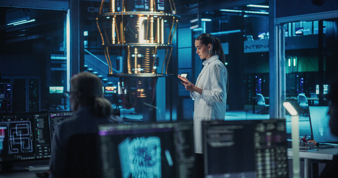 Portrait of a Female Researcher Standing Before a Powerful Quantum Computer, Using a Tablet Computer to Monitor Digital Data. Smart Woman  is Analyzing Results and Parameters Online