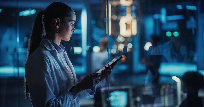 Female Scientist Using a Tablet to Monitor the Work of a Quantum Computer, Focusing on Data Flow, Compute and Hardware Stability. Futuristic Dark Setting with Advanced Technological Office