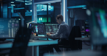Caucasian Quantum Computer Engineer Working in a Dark Office in an Advanced Computer Research and Development Facility. Young Male Programming the Work and Data Flow of a Quantum Computer