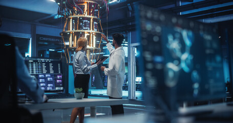 Middle Aged Female and Young Indian Male Working in a Research Laboratory with a Quantum Computer....