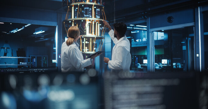 Female and Male Engineers Collaborating on Quantum Computer Development, Discussing a Report on a Tablet Computer in a Research Center. Colleagues Focusing on Innovation and Technology Breakthroughs