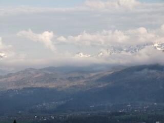Golden light at sunset touches forested hills and cloud-covered snowy Tatra Mountains, with Zakopane town visible below from Gubalowka viewpoint