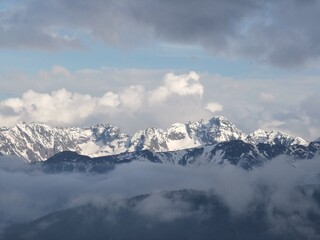 Majestic snow-covered Tatra Mountains piercing through layers of clouds and mist, seen from Gubalowka Hill in Zakopane under dramatic sky