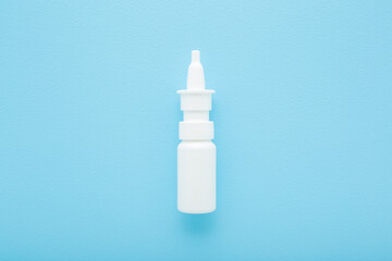 New white plastic spray bottle of medical liquid to stop nose running on light blue table background. Pastel color. Closeup. Top down view.