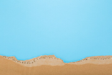 Torn light brown carton on light blue table background. Pastel color. Closeup. Empty place for...