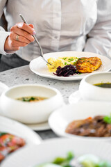 A person holds a fork, ready to enjoy a plate of creamy mashed potatoes and a delicious fritter, with other gourmet dishes visible in the background, showcasing a delightful dining experience.