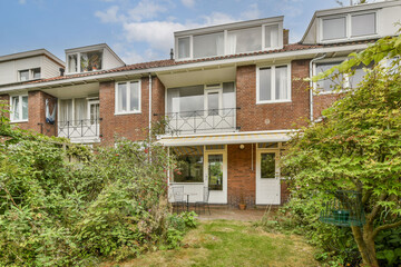 A contemporary multi-level residential building featuring a brick facade, large windows, and a vibrant garden area with lush greenery and well-maintained shrubs.