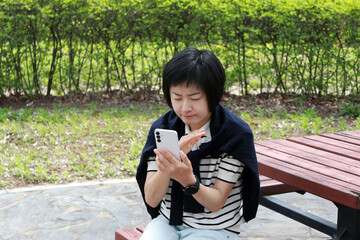 An Asian woman wearing a striped white knitwear with a navy cardigan on her shoulder and making a video call with her smartphone.
