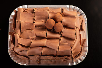 Chocolate cake, close-up of a chocolate cake decorated with rolled chocolate shavings and sprinkled cocoa truffles on a silver tray over a dark surface, selective focus.