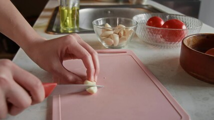 Zoom out rack focus shot of unknown girl taking clove of garlic from little bowl and cutting it on plastic chopping board