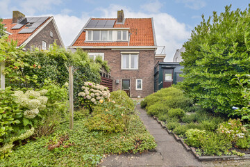 This image showcases a charming house surrounded by a vibrant garden filled with various plants, flowers, and well-kept greenery, highlighting an inviting residential atmosphere.