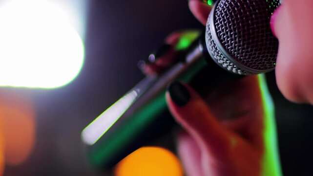 Beautiful girl lips and mouth close-up singing into microphone on stage against colorful lights background, artist, slow mo