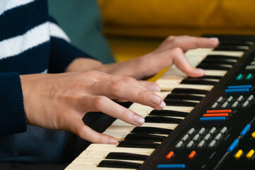 Obraz premium Woman composer sitting on a comfortable sofa, playing a vintage synthesizer keyboard and creating electronic music in a cozy home environment filled with inspiration and creativity