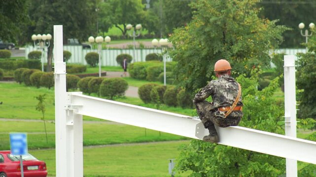 A male fitter at a construction site assembles a metal structure at a construction site in the summer. Danger at height, copy space for text