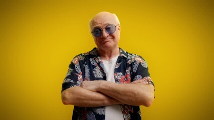 Stylish grandpa in sunglasses folding arms and smiling on yellow background