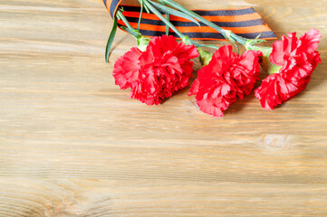 9 May background, Victory Day card. Three red carnations and St George ribbon lying on the wooden...