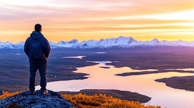 Man admires breathtaking sunset over serene mountain lake and snow-capped peaks