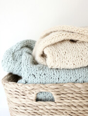 Pastel-colored knitted blankets stacked in basket on white background