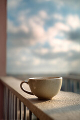 Obraz premium A white coffee cup sits on a railing, with a cloudy sky in the background