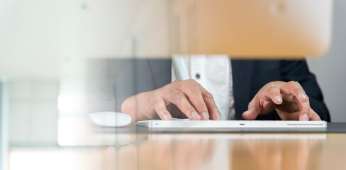 Closeup of Indian businessman typing on keyboard and scrolling mouse at desk in office.