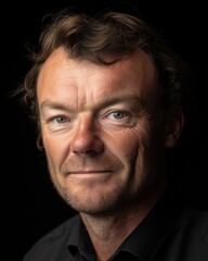 Fototapeta premium A middle-aged man with short hair and a serious expression against a dark background.