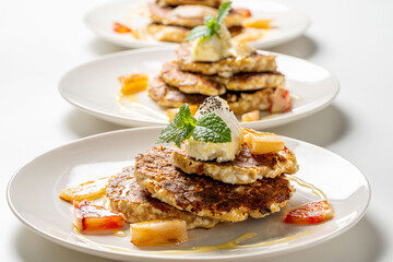 Healthy, dietary breakfast. Cottage cheese pancakes with cream cheese, orange, honey and mint on a white plate and background.