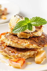 Cottage cheese pancakes with honey, orange, mint and cream are decorated with mint on a white plate. The concept of a delicious and healthy dietary breakfast. Close-up.