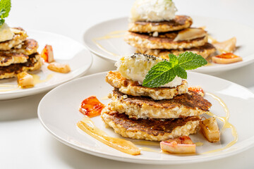 Cottage cheese pancakes with honey, orange, mint and cream are decorated with mint on a white plate. The concept of a delicious and healthy dietary breakfast. Close-up.