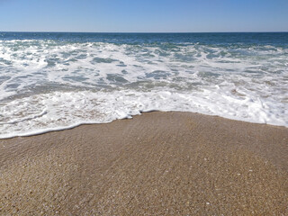 A serene beach at midday with gentle waves lapping the shore and clear blue skies inviting relaxation