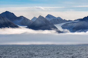 Glaciers and mountains of Konsfjorden, Svalbard. Low cloud is hugging the coastline with the peaks rising above the cloud line.