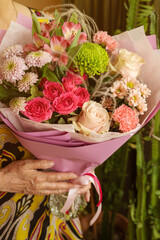Elderly woman hands hold withered dry old rose flowers bouquet, contrast image. Old age, infirmity, withering, wrinkles concept