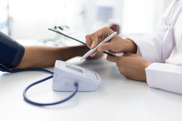 Fototapeta premium Female doctor measuring blood pressure of patient in hospital room. Doctor using sphygmomanometer checking blood pressure of patient during medical exam in clinic, healthcare and medical concept.