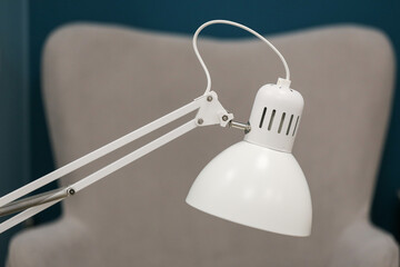 White desk lamp. Minimalist design. Modern workspace light. Metal lamp focus. Home office detail. Interior lighting. Simple lamp arm. Clean room background. Stylish office setup. Bright light tool.