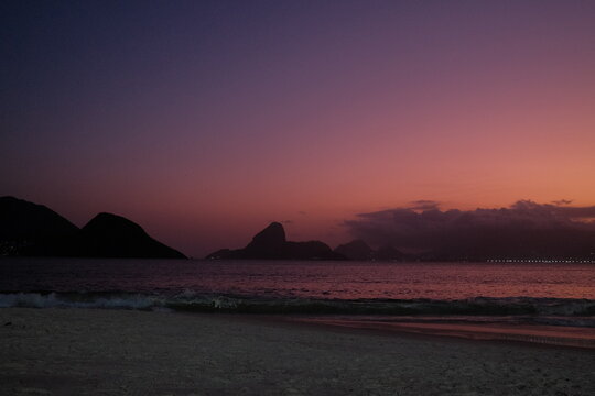 P&ocirc;r do sol vibrante na Praia de Icara&iacute;, em Niter&oacute;i, com vista para o P&atilde;o de A&ccedil;&uacute;car, Ba&iacute;a de Guanabara e o skyline do Rio de Janeiro sob tons de rosa, roxo e laranja.