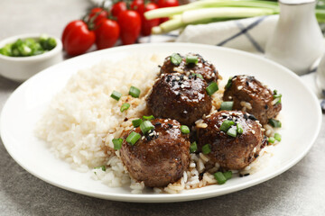 Delicious rice with meatballs, sauce and green onions on grey table, closeup
