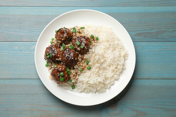 Delicious rice with meatballs, sauce and green onions on blue wooden table, top view