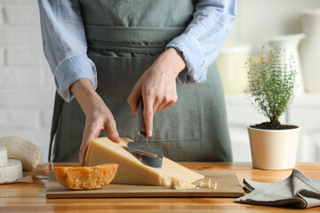 Woman cutting delicious cheese with slicer at wooden table indoors, closeup