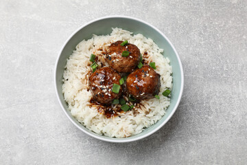 Delicious rice with meatballs, sauce and green onions in bowl on grey table, top view