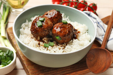 Delicious rice with meatballs, sauce and green onions on white wooden table, closeup