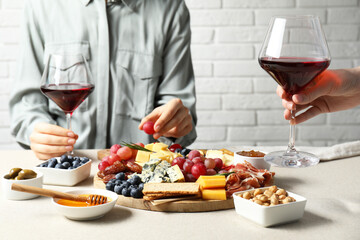 Women holding glasses of wine at light grey table with different snacks indoors, closeup